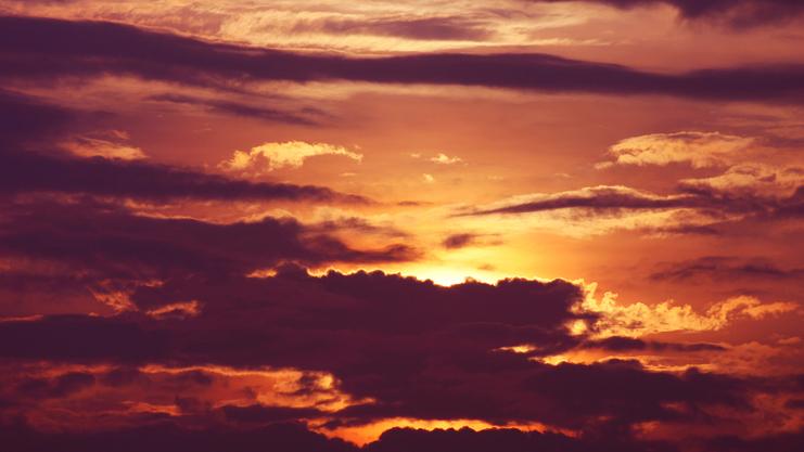 Farbenfroher Sonnenuntergang hinter bewölktem Himmel mit orangefarbenen und violetten Tönen.