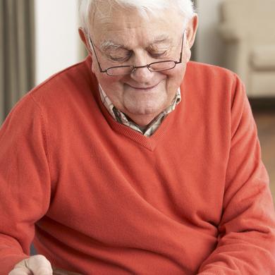 Älterer Mann in rotem Pullover hält einen Bilderrahmen und lächelt, während er ihn betrachtet. Natürliche Wohnatmosphäre.